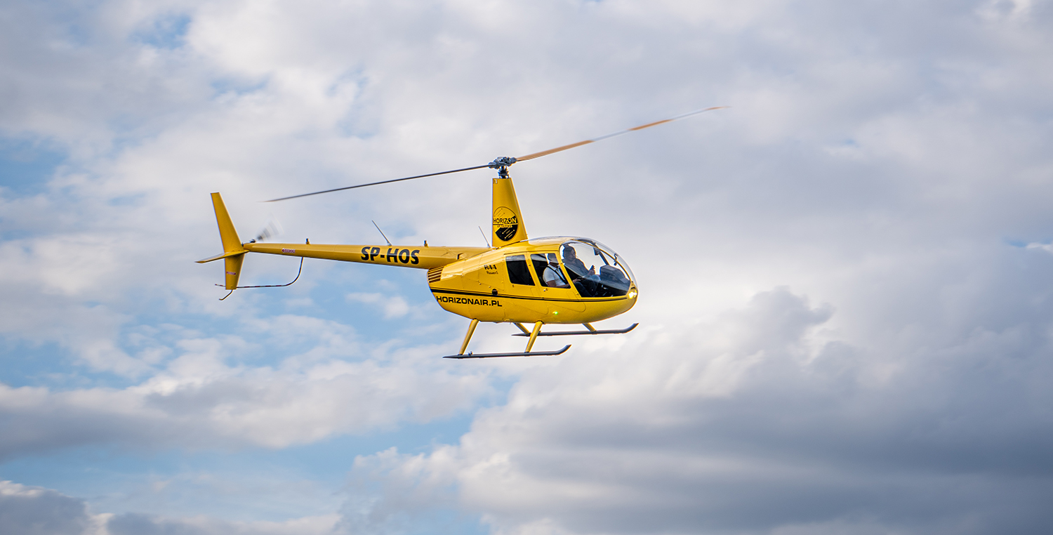Żółty helikopter w locie na tle chmur.